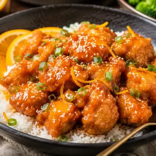 Crispy air fryer orange chicken tossed in glossy orange sauce with rice and sesame seeds