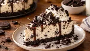 Slice of no‑bake Oreo cheesecake on a plate with whipped cream and Oreo pieces
